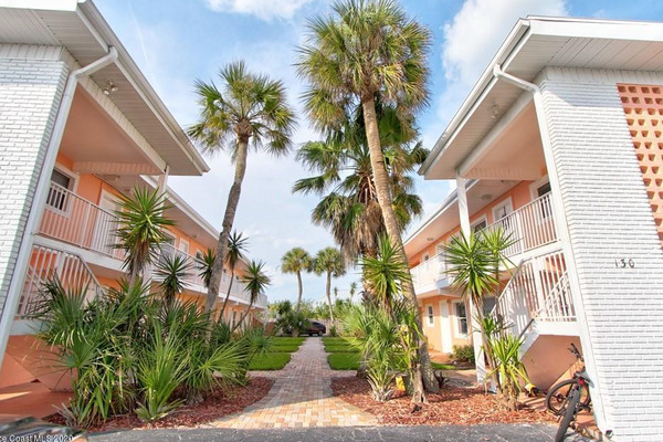 peach and white condo buildings with palm trees in between 