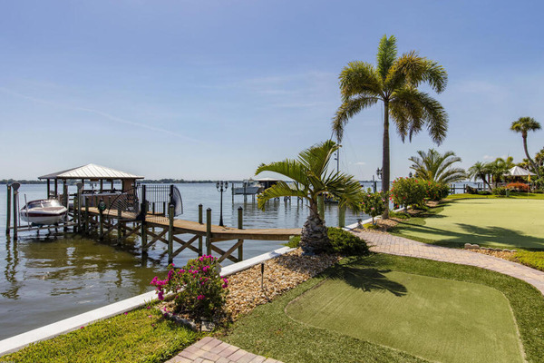 covered dock and boat lift on river behind luxury home yard