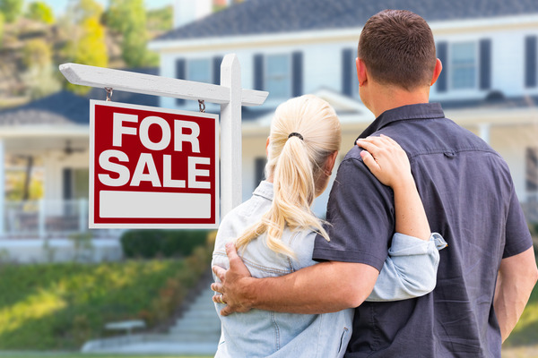 man and woman look at house with for sale sign in front