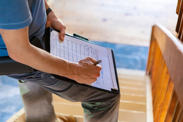 Man on stairs marking checklist on clipboard against his leg