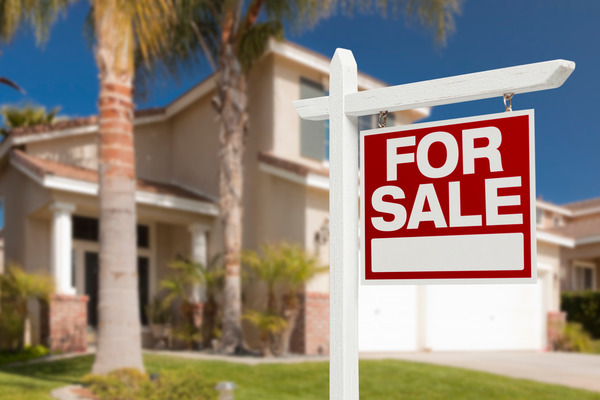 Red for sale sign in front of house with palm trees