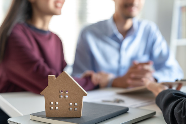 Couple discusses home purchase with cute home model in front