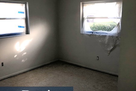 Bedroom #1 after removal of carpet and after a coat of primer paint to cover the blue walls. Builder grade ceiling fixture removed.