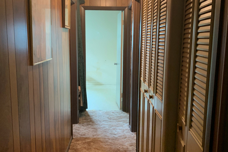 Cave like is the best way to describe the original hallway that leads to home's bedrooms. Dark wood paneling, brown bi-fold doors, brown door casings and dark carpet were original to the home.