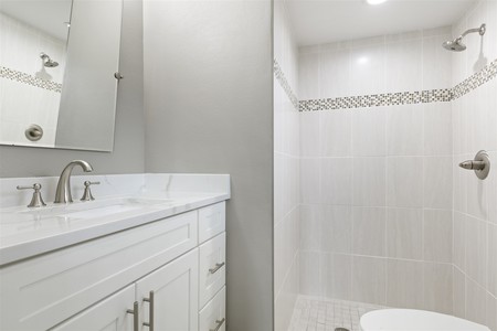 After - Large neutral color tile in the shower, white shaker vanity, quartz counter top and new white toilet and brushed nickle fixtures lighten and brighten the room