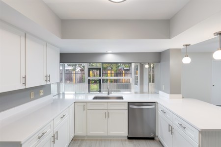 After - Crisp white quartz counters, neutral beige walls and flooring as well as simple ceiling light instead of drop ceiling and pendant lighting opens the kitchen space 