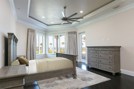 First master bedroom with recessed tray ceiling, neutral wall color and Banana River views as well as pool deck access.