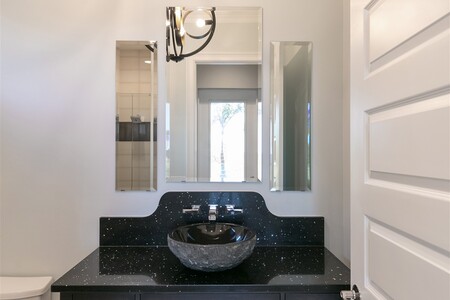 Pool bathroom includes vessel sink on black granite vanity and river rock flooring shower.
