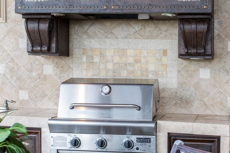 Summer kitchen cabinetry also features the rich brown faux finish and golden accents seen in the hood detail. There is also decorative tile backsplash across the counter space.