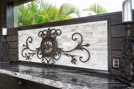 Cabana detail of accent wall with shelf features decorative iron work on a backdrop of stacked stone and rustic wood.