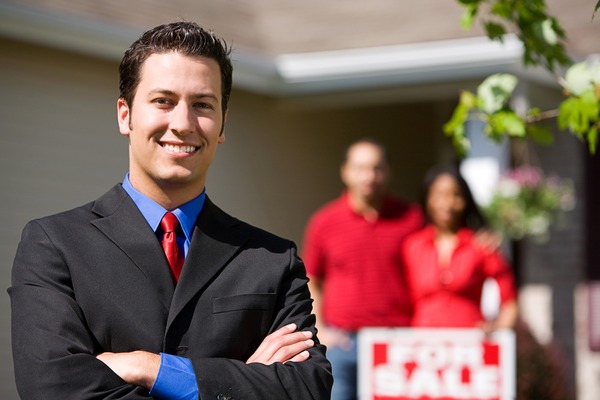realtor with background of couple with for sale sign
